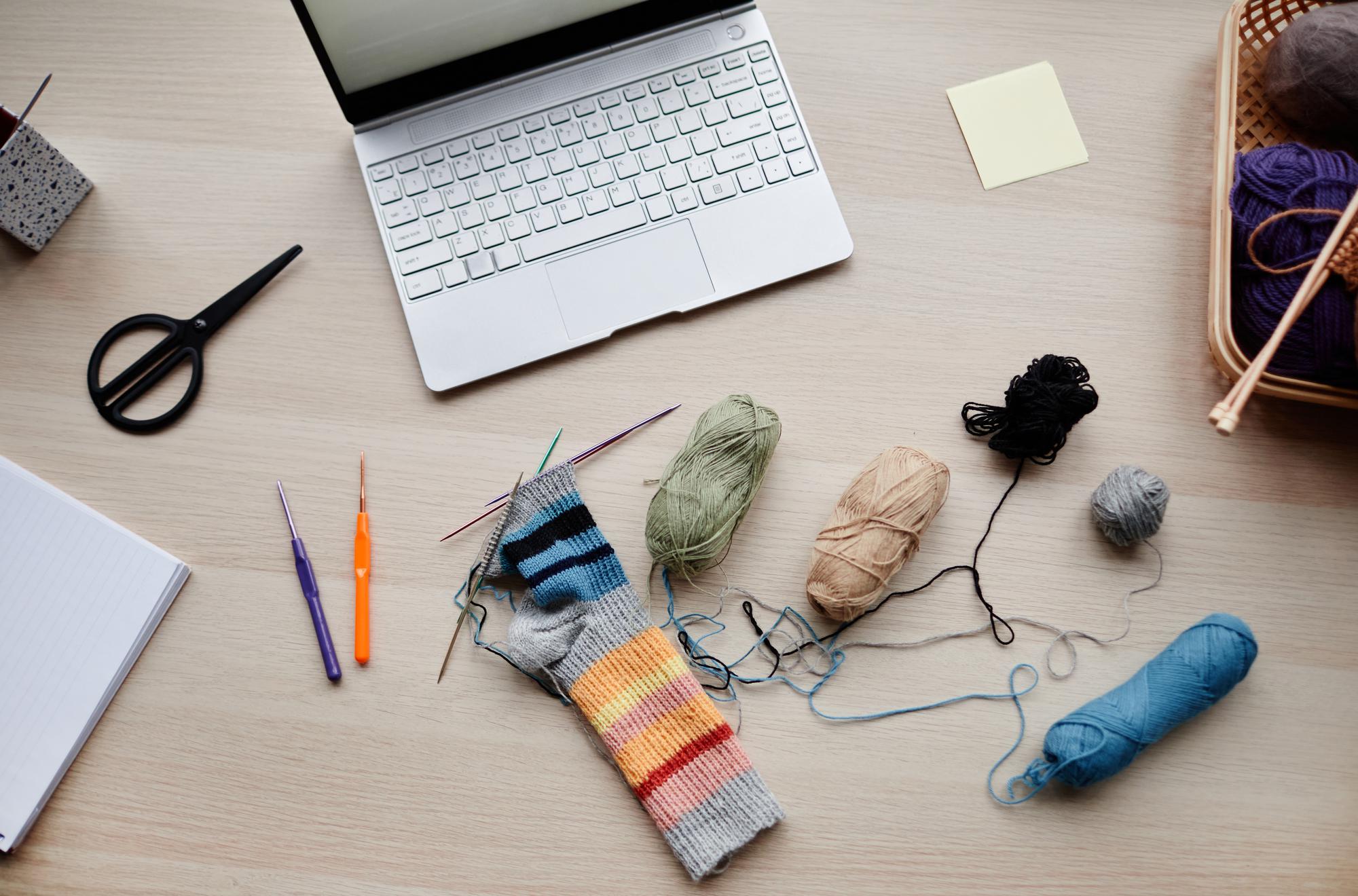 Studio table with threads, hoops and laptop showing embroidery pattern